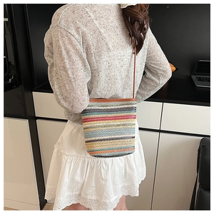 Détail d'un sac seau en paille à rayures colorées avec bordure et bandoulière en cuir brun