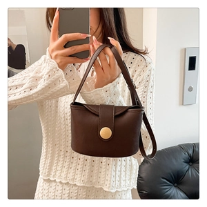 Detail view of deep brown leather bucket bag with a golden round clasp and thin shoulder strap