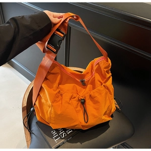 Detail of orange nylon crossbody bag featuring drawstring pocket and buckle strap