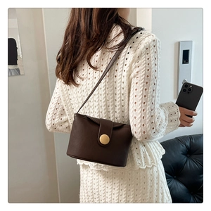 Close-up of brown faux leather bag with gold circular buckle and magnetic flap