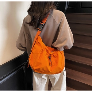 Detail of bright orange drawstring crossbody bag with adjustable strap and black buckle