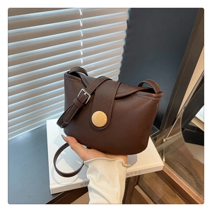 Detail of soft brown leather bag featuring circular wood-texture buckle and metal strap buckle
