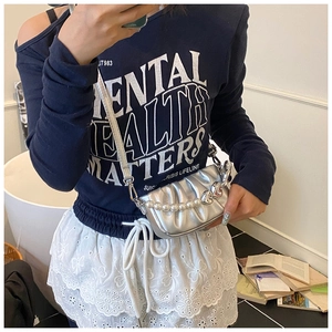Detail of silver pleated crossbody bag with pearl heart chain worn by a model