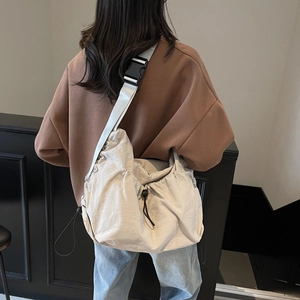 Detail of off-white nylon crossbody bag with drawstring closure and adjustable gray strap