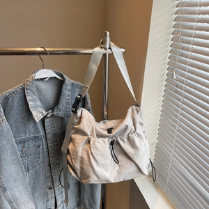 Detail of light gray nylon crossbody bag with drawstring closure and wide adjustable strap
