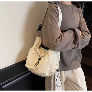 Detail of cream drawstring pleated bag with wide shoulder strap and black buckle closure