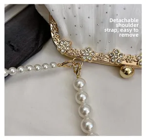 Détail de la bandoulière perle amovible et du fermoir fleuri en strass sur la pochette blanche