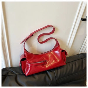 Detail of red patent leather shoulder bag with side pockets on black leather surface