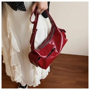Close-up of wine red multi-pocket shoulder bag with glossy finish and wide strap