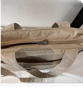 Detail view of khaki tote bag featuring smooth metal double zippers and reinforced handles
