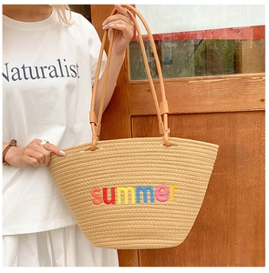 Detail of hand-woven beige tote bag featuring colorful summer embroidery and slim handles
