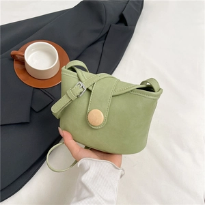 Green soft leather crossbody bag with a round button buckle shown in a lifestyle setting