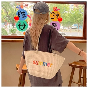 Detail of hand-woven beige tote bag featuring colorful summer embroidery on the front