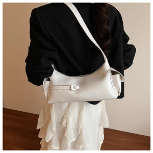 Detail of a minimalist creamy white baguette bag worn by a model in a black suit