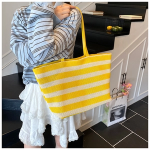 Detail of yellow and white striped woven tote bag with long straps on a female model
