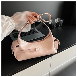 Detail of light pink glossy patent leather shoulder bag on a desk with laptop