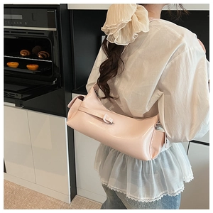 Gros plan d'un sac à bandoulière cylindrique en cuir verni rose clair dans une cuisine