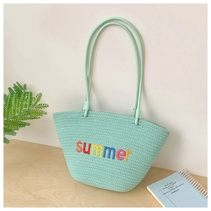 Detail of mint green woven tote bag with colorful Summer embroidery on a wooden table