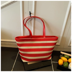 Detail of red and white striped knit tote bag with red leather straps in a lifestyle setting