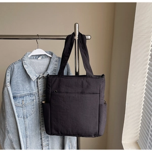 Detail of black canvas tote bag with front zip pocket hanging on a rack in a room