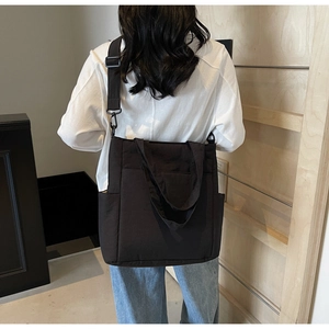 Detailed back view of a minimalist black canvas crossbody bag shown on a female model
