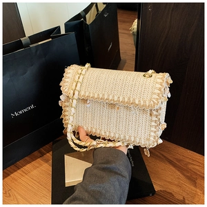 Gros plan sur sac en paille tressée crème avec détails coquillages et chaîne