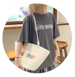 Detail of white woven tote bag with summer embroidery and thin handles on model