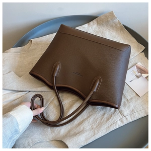 Detail of brown leather tote bag with pebble texture and debossed fashion logo on front