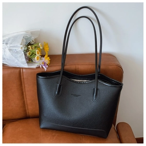 Close-up of black pebble leather tote bag with embossed fashion text on a leather sofa