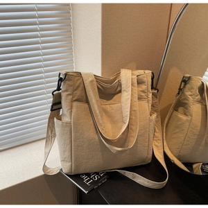Detail view of beige nylon tote bag showing front pocket and adjustable shoulder strap