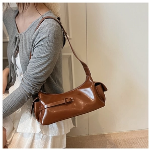 Detail of a brown glossy patent leather shoulder bag with decorative buckle and side pocket