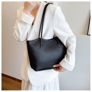 Close-up of minimalist black pebbled leather tote bag worn over the shoulder by a model