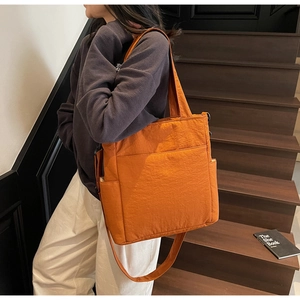 Close-up of orange nylon tote bag with large front pockets and adjustable crossbody strap