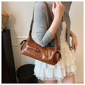 Close-up of brown glossy faux leather shoulder bag with buckle and side pockets