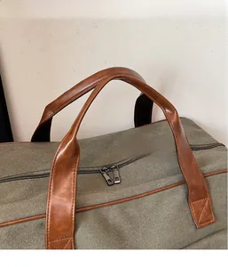 Detail of military green canvas travel bag with brown leather handles and dual zippers