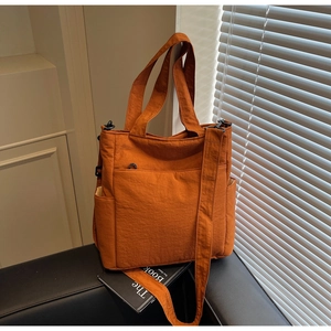 Detail of caramel canvas tote bag showing side pocket and wide strap on leather chair