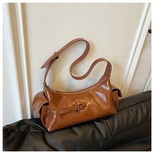 Detail of a brown glossy leather shoulder bag with side flap pockets and adjustable strap