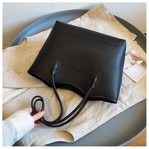 Detail of black pebbled leather tote bag with thin straps and minimalist embossed logo