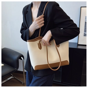 Detail of a large cream tote bag with brown leather trim worn as a stylish shoulder bag