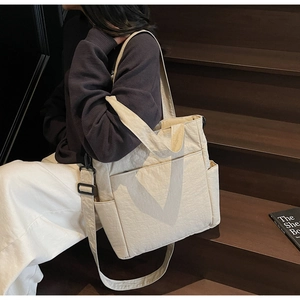 Detail of off-white nylon tote bag with multiple pockets and wide strap on steps