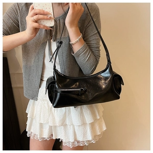 Model wearing a glossy black underarm bag with double pockets and retro cargo design