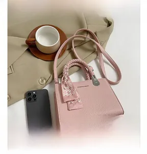 Detailed shot of pink litchi grain handbag with woven handle and plaid silk scarf decoration