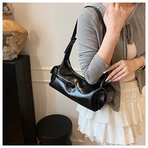 Glossy black baguette bag with adjustable strap and metal zippers shown on a model