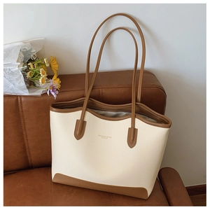 Close-up of cream textured leather tote bag with brown handles on a leather sofa