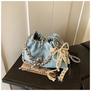 Detail of light blue denim bucket bag with silver chains, pearls and a lace bow