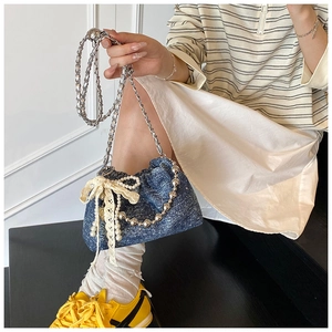 Detail of dark blue denim drawstring bag with lace bow and pearl chain charm