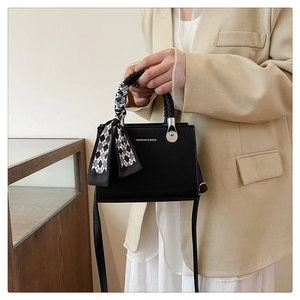 Detail of black leather square bag with woven handle and elegant silk scarf decoration