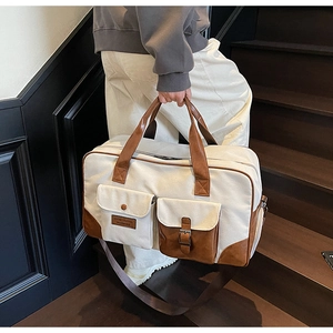 Detail of canvas travel bag featuring brown leather trim and large front pockets