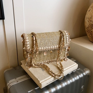 Sac bandoulière en paille avec breloques coquillages et pompons sur une valise