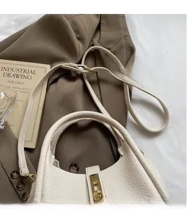 Détail de la texture cuir crème, du fermoir doré et de la bandoulière réglable du sac